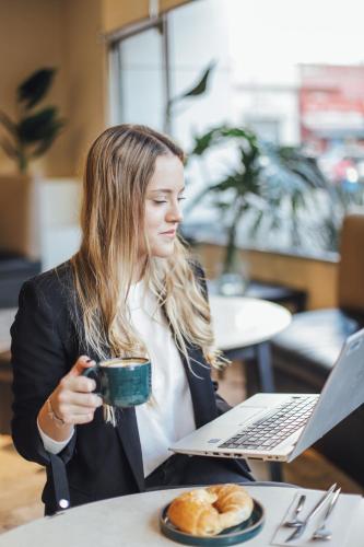 a woman sitting at a table with a cup of coffee and a laptop at Plaza Real Suites Hotel in Rosario