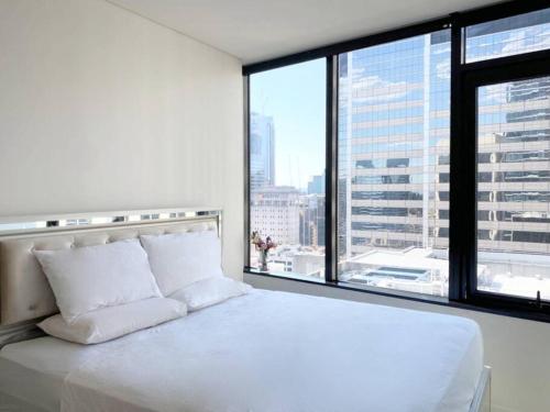 Cette chambre comprend un lit blanc et une grande fenêtre. dans l'établissement Sydney CBD Luxury Furnished Apartment & City Views, à Sydney