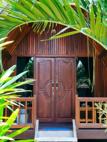 a wooden door of a house with a palm tree at Leaf Coco Bungalow in Gili Air