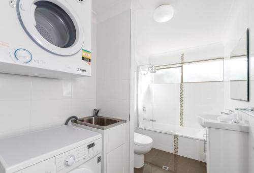 bagno bianco con lavandino e lavatrice di The Hidden Flower - A Spacious Poolside Abode a Brisbane