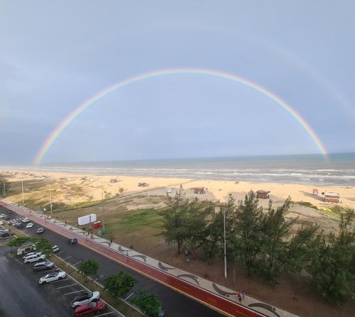 a rainbow over a road and a beach with cars at Apartamento Beira mar Capão da Canoa in Capão da Canoa