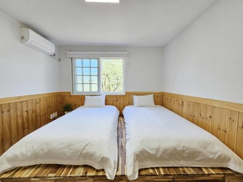 dwa łóżka w pokoju z oknem w obiekcie Baerongnamu Private Stay w mieście Seogwipo