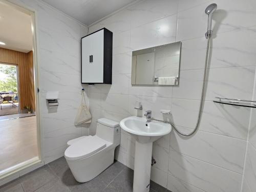 a white bathroom with a toilet and a sink at Baerongnamu Private Stay in Seogwipo