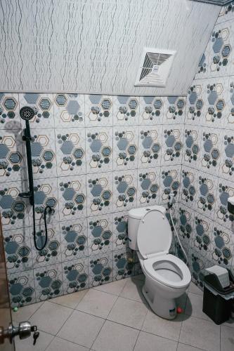 a bathroom with a toilet and a tile wall at Golden Orchid Villa in Dieng