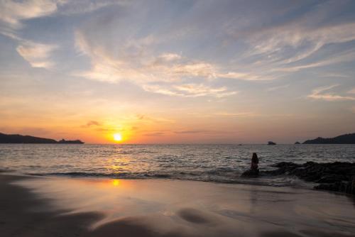 a person standing on the beach watching the sunset at Andaman Beach Hotel Phuket - Handwritten Collection in Patong Beach