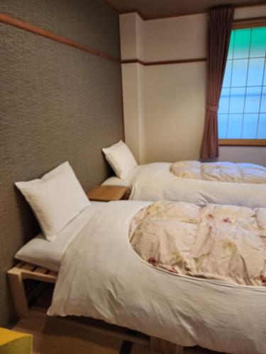 a bedroom with two beds with white sheets and a window at Hakuba Hotel Hana-no-Sato in Hakuba