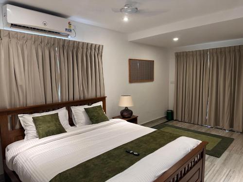a bedroom with a large bed with white sheets and green pillows at Villa Ithaka by Youkoso in Chennai