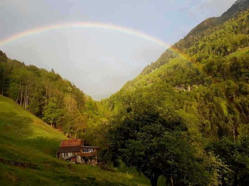 einen Regenbogen über einem Haus in einem grünen Tal in der Unterkunft Panorama Jurte über dem Uri-See B in Sisikon