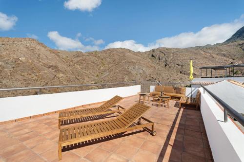 a deck with chairs and tables and mountains in the background at Vivienda vacacional La Era Il in Vallehermoso