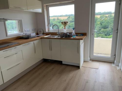 a kitchen with white cabinets and a sink and a window at Sea Breeze Wembury Beach in Wembury