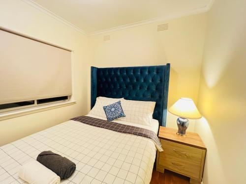 a bedroom with a bed with a blue headboard and a lamp at Cosy Homes - 15 Minutes Away From Melbourne Airport in St Albans