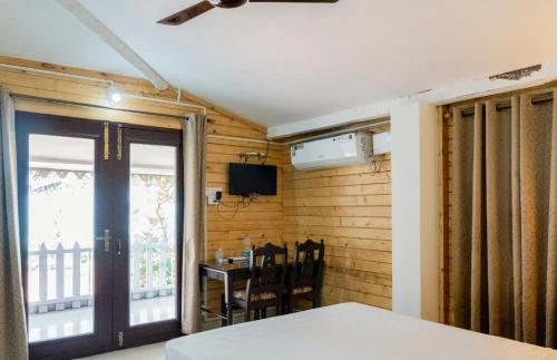 Habitación con puerta, mesa y balcón. en Peles Windsong wooden cottages, en Benaulim