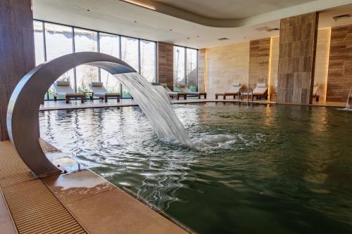 a pool with a water fountain in a building at Anadolu Hotels Esenboga Thermal in Esenboga