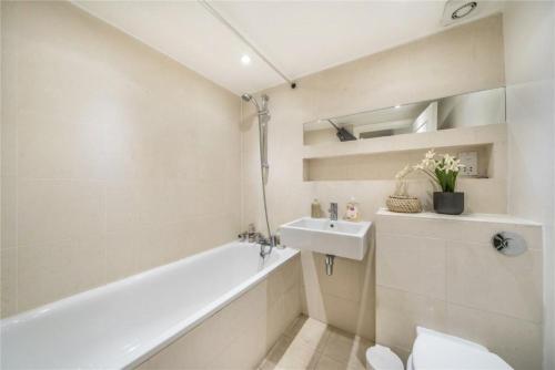 ein Badezimmer mit einer weißen Badewanne und einem Waschbecken in der Unterkunft BOND STREET STATION 2 BED FLAT in London