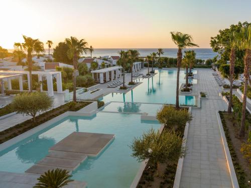 an overhead view of a pool with palm trees and the ocean at Grecotel Lux Me Dama Dama in Faliraki