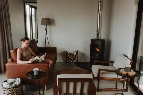 a woman sitting in a chair reading a book in a living room at Spionkop Eco Cabin in Reddersburg