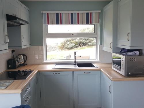 a kitchen with white cabinets and a sink and a window at White Ocean in Mawgan Porth