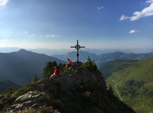 two people sitting on top of a mountain with a cross at Wellnessappartements Margit in Alpbach