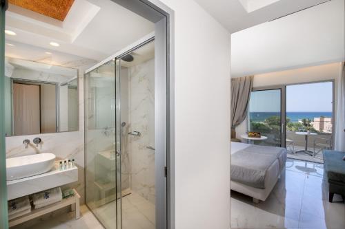 a bathroom with a shower and a sink and a bed at Vantaris Luxury Beach Resort in Georgioupolis