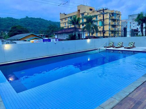 a swimming pool with two chairs and a building at Lindo apto na Enseada - Guarujá - 8 min da praia in Guarujá