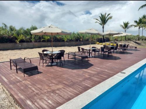 eine Terrasse mit Tischen, Stühlen und Sonnenschirmen neben einem Pool in der Unterkunft Praia da Pérola in Ilhéus