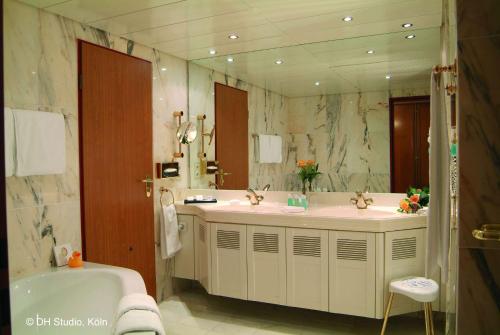 a bathroom with two sinks and a tub and a mirror at Maritim Airport Hotel Hannover in Hannover