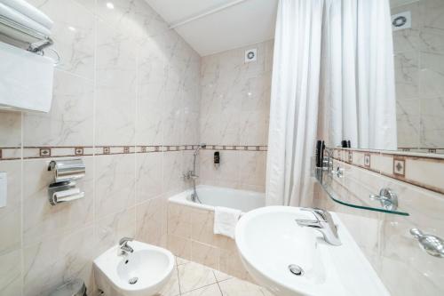 a white bathroom with a sink and a bath tub at Hotel Raffaello Prague in Prague