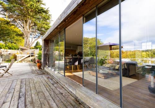 a house with glass walls and a wooden deck at Chalon - A quirky hideaway on the river for 2 in Cardigan