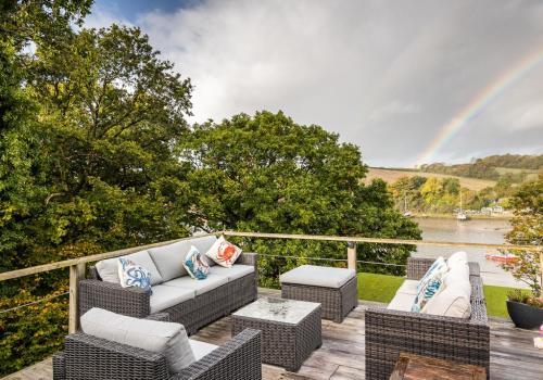 a patio with a couch and chairs on a deck with a rainbow at Chalon - A quirky hideaway on the river for 2 in Cardigan