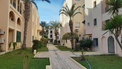 une passerelle entre deux bâtiments plantés de palmiers dans l'établissement Appartement résidence Port yasmine hammamet, à Hammamet