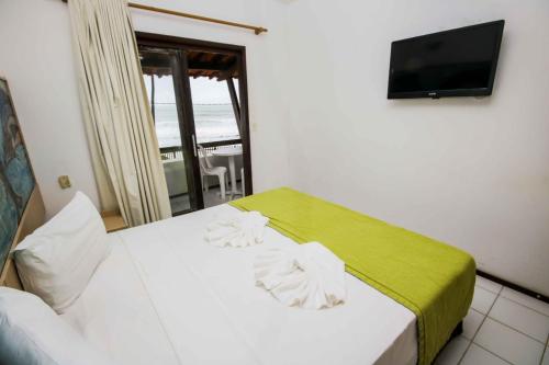 a bedroom with a bed with a green blanket and a television at Pousada Caravelas de Pinzón in Cabo de Santo Agostinho