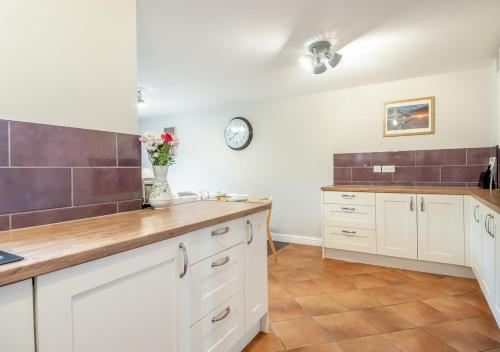 a kitchen with white cabinets and a clock on the wall at Pebble Cottage in Little Walsingham