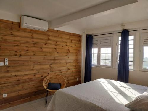 ein Schlafzimmer mit einer Holzwand mit einem Bett und einem Stuhl in der Unterkunft VILLA MARIE in Marigot
