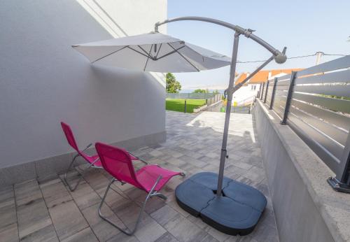 two pink chairs and an umbrella on a balcony at Apartments Luka in Senj