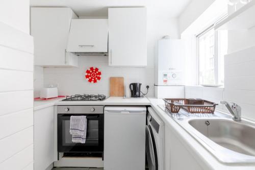 - une cuisine blanche avec évier et cuisinière dans l'établissement Cosy 1bedroom Flat - 2 Min Walk to Kensington Gardens!, à Londres
