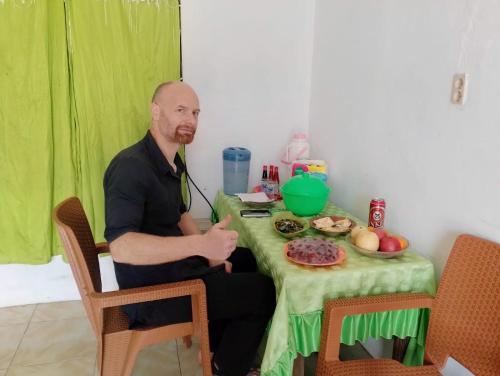 um homem sentado numa mesa com uma toalha de mesa verde em Penginapan Kofiyau em Sorong