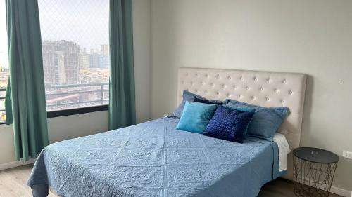 Un dormitorio con una cama con almohadas azules y una ventana en Mesquita Arriendos - Departamento full amoblado para 7 personas, en Iquique