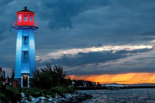 a lighthouse on the water with a sunset in the background at Cozy Condo at the Lake in Sylvan Lake