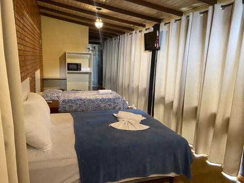 a room with two beds with curtains and a blue table at Suites Aconchego do Centro - Localizado no Centro in Canela