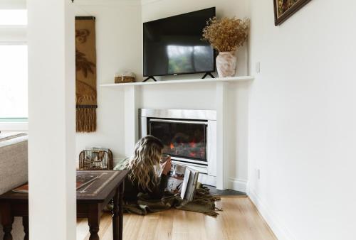 a woman sitting on the floor in front of a fireplace at Hey Little Joe - Cosy Retreat with Mountain Views in Warburton
