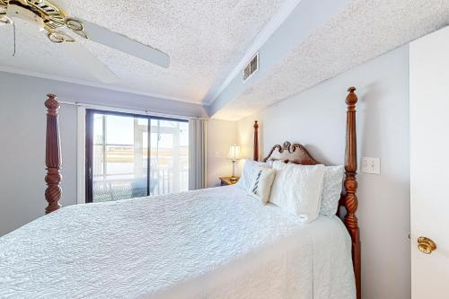 a bedroom with a bed with white sheets and a window at A Place Between the River and Sea in North Topsail Beach