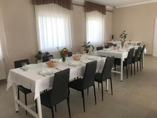 jadalnia z białymi stołami i czarnymi krzesłami w obiekcie Vállaj Vendégház 