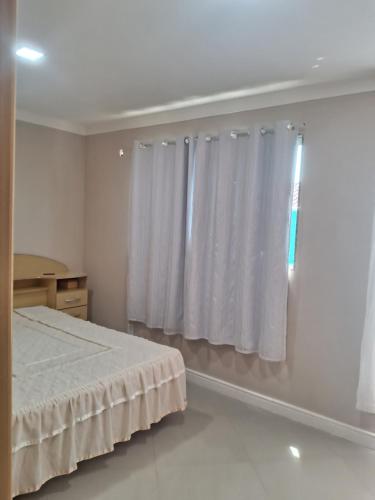 1 dormitorio con 1 cama y una ventana con cortinas blancas en Casa para temporada em Rio das Ostras, en Rio das Ostras