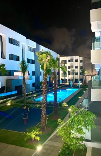 uma piscina com palmeiras em frente a um edifício em Belle appartement à découvrir em El Harhoura