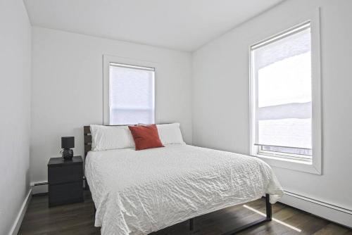 a white bedroom with a bed and two windows at Downtown Prestige: Parking, King Bed, Sleeps 6 in Sherbrooke