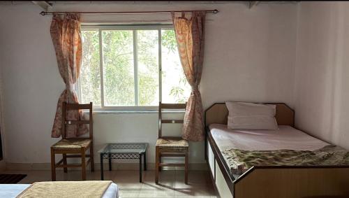 a bedroom with a bed and a window and two chairs at Perfect Couple Bedroom in Panchgani