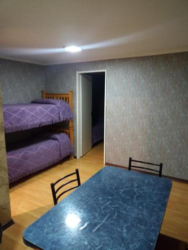Habitación con mesa y dormitorio con camas de color púrpura. en Hospedaje "San Andres" en Gobernador Gregores