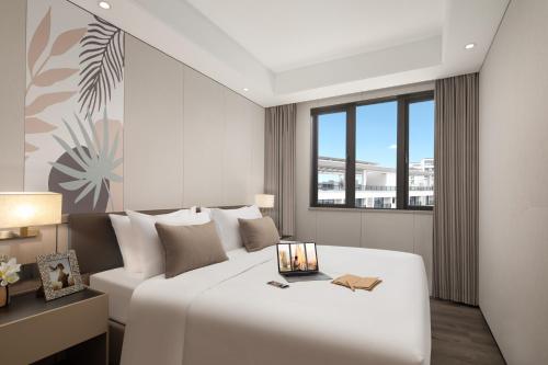 a bedroom with a large white bed and a window at Citadines Hope City Boao in Qionghai