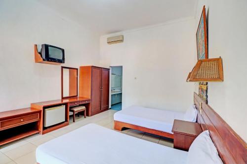 a bedroom with a bed and a desk and a tv at Capital O 93236 Hotel Hapel Negara in Banyubiru