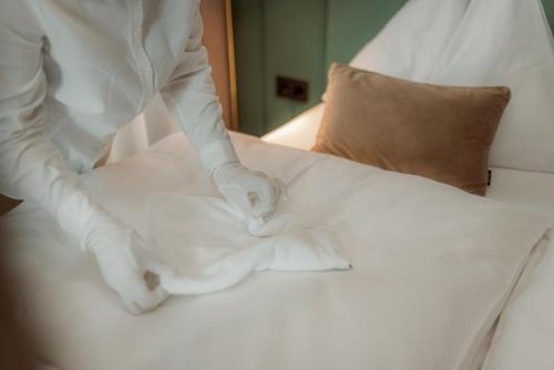 a person in gloves making a bed with white sheets at NED Hotel in Graz